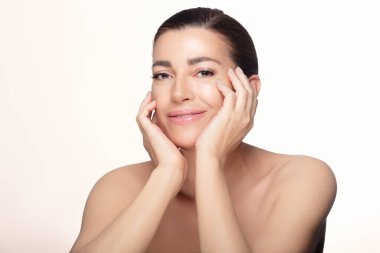 Parlak tenli, güzel orta yaşlı kadın doğal bir şekilde poz veriyor. Güzellik ve cilt konseptini gösteriyor. Kopyalama alanı olan hafif bir arkaplanda izole edilmiş.