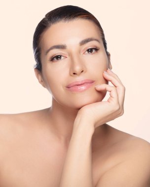 50 'li yaşlarda, parlak tenli, eli çenesinde poz veren, cilt bakımı için poz veren güzel doğal bir kadın. Arka planda izole edilmiş. Boşluğu kopyala.