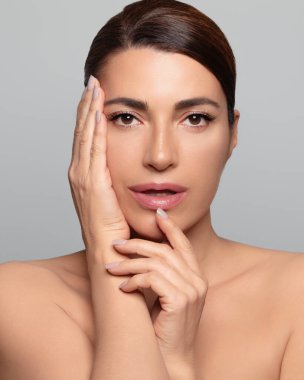 Cildi kusursuz ve doğal makyajı cildini geliştiren orta yaşlı güzel bir kadın. Güzellik ve kozmetoloji reklamları için ideal. Gri arkaplanda dikey biçim izole edildi.