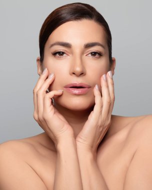 Yüzüne doğal makyajla dokunan güzel bir kadının yakın çekimi. Mükemmel cilt ve nötr gri arka plan. Gri arkaplanda dikey biçim izole edildi