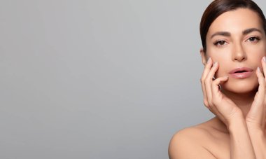 Doğal cilt bakımı ve güzellik sergileyen orta yaşlı güzel bir kadın. Kozmetoloji reklamları için ideal. Geniş kopyalama alanı olan yumuşak gri bir arkaplan ile izole edilmiş.