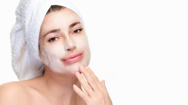 Yüzüne maske ve havlu sarılmış bir kadın yüzüne dokunuyor. Güzelliğin, cilt bakımının ve sağlığın mükemmel bir temsili. Tasarım ihtiyaçları için kopyalama alanı olan dikey biçim.