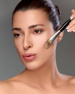 Bir kadın ustalıkla makyaj yapıyor, bir fırçayla, güzellik ve cilt bakımını vurguluyor. Görüntü zarafet ve hassasiyet yayar..