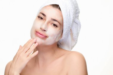 Yüzüne maske ve havlu sarılmış bir kadın yüzüne dokunuyor. Güzelliğin, cilt bakımının ve sağlığın mükemmel bir temsili. Tasarım ihtiyaçları için kopyalama alanı olan dikey biçim.