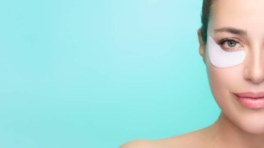 Göz bantlı bir kadının portresi, cilt bakımını ve sağlığını destekliyor. Sakinleştirici mavi arka plan, sakin bir spa havası katıyor. Kopyalama alanı ile izole edilmiş.
