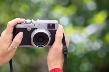 Yakından bakınca, elinde geçmişe dönük bir kamera olan birini, bulanık yeşil bir arkaplanda görüyoruz. Kamera nostalji ve yaratıcılık hissi uyandırıyor. Yatay biçim.