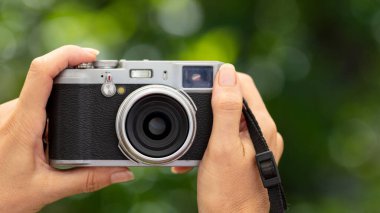 Arka planda bulanıklık olan eski tarz bir kamera tutan ellerin yakın çekimi. Fotoğrafçılığı ve nostaljiyi vurguluyor. Yaratıcı projeler için mükemmel. Yatay biçim.