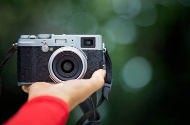 Yeşil bokeh arka planına karşı el ele tutuşan retro biçimli dijital kamera.