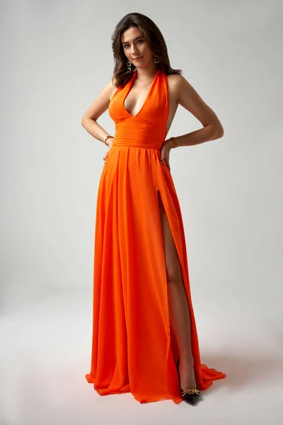 Сексуальная Модель Оранжевом Платье Демонстрирующая Ногу Сером Фоне — стоковое фото