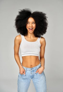 Gülümseyen kadın portresi diş telleri ve gri arka planda izole edilmiş afro saç stili.