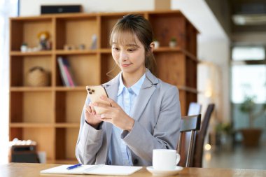 Kafedeki akıllı telefona bakan Asyalı kadın.