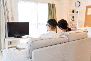 Oturma odasında televizyon izleyen Asyalı çift.