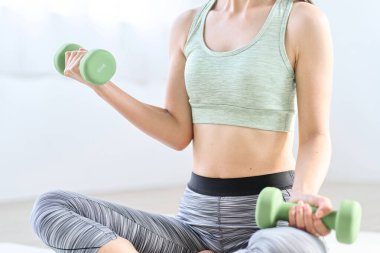 Asyalı kadın evde dambıl eğitimi yapıyor.