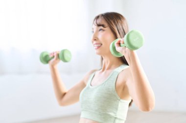 Asyalı kadın evde dambıl eğitimi yapıyor.