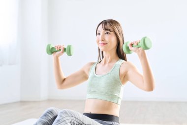 Asyalı kadın evde dambıl eğitimi yapıyor.