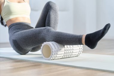 Dizlerinin arkasını gevşetmek için köpük rulo kullanan bir kadın.