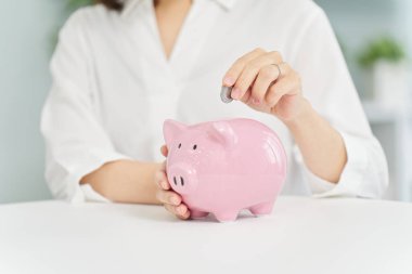 Bir kadın domuz kumbarasına para yatırıyor.