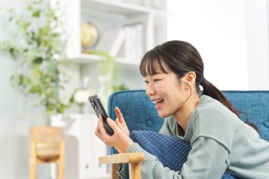 Kanepede uzanmış akıllı telefonuna bakan bir kadın.