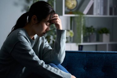 Karanlık bir odada başını tutan bir kadın.