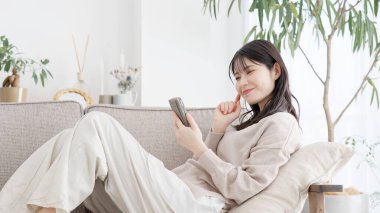 Kanepede dinlenen ve akıllı telefonuna bakan bir kadın.