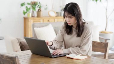 Evdeki bilgisayar ekranına bakarken not alan bir kadın.