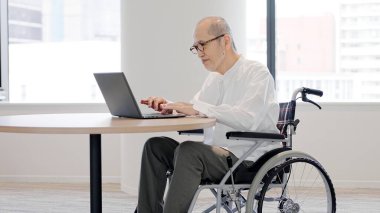 Elderly person in a wheelchair operating a computer clipart