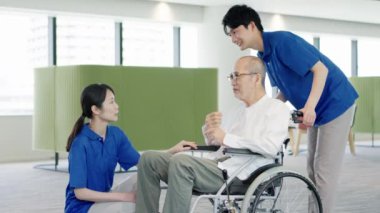 Tekerlekli sandalyedeki yaşlı kişi bakıcısıyla konuşuyor.