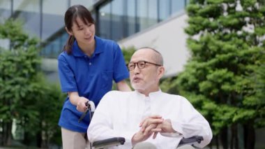 Tekerlekli sandalyedeki yaşlı insanlar bakıcılarıyla yürüyüşe çıkıyorlar.