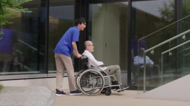 Tekerlekli sandalyedeki yaşlı kişi ve merdivenlerde duran bakıcı.