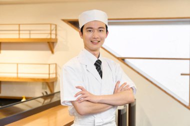 A Japanese chef with his arms folded inside the restaurant clipart