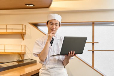 Japon bir şef dizüstü bilgisayar tutuyor ve endişeleniyor.