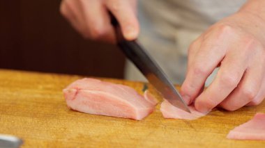 Suşi şefinin elleri yağlı ton balığını kesiyor.