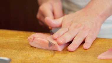 Suşi şefinin elleri yağlı ton balığını kesiyor.