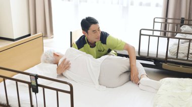 Asian caregiver changing the position of an elderly person