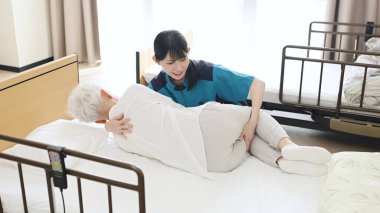 Asian caregiver changing the position of an elderly person