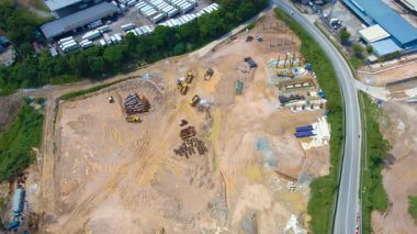 Eğri bir yol ve yeşillikle çevrili, makineler, malzemeler ve temel çalışmaları olan bir inşaat alanının havadan 4K görüntüsü. Altyapı projeleri için ideal.