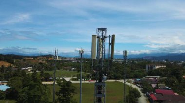 Yeşil ve uzak dağlarla çevrili bir banliyö bölgesinin üzerinde yükselen 5G antenlerinin havadan 4K görüntüsü. Haberleşme ve teknoloji projeleri için ideal.