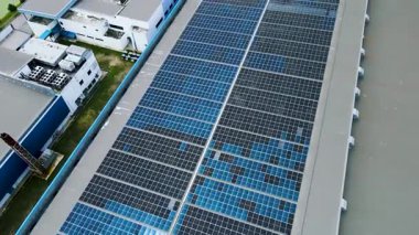 Çatıda güneş panelleri olan büyük bir endüstriyel binanın havadan 4K görüntüsü. Temiz enerji ve sürdürülebilirliği teşvik eder.