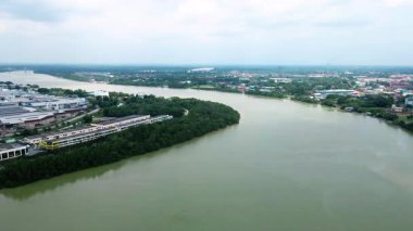 Nehir kıyısında yemyeşil mangrov ağaçları ve endüstriyel binaları olan bir şehir kasabasından akan geniş bir nehrin havadan görünüşü. Yukarıdan huzurlu su manzarası.