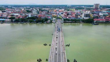 Nehirden geçen uzun bir köprünün insansız hava aracı görüntüsü. Arabalar her iki yöne de hareket ediyor. Binaları ve liman faaliyetleri olan canlı bir şehir merkezine gidiyor..