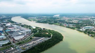 Nehir kıyısında yemyeşil mangrov ağaçları ve endüstriyel binaları olan bir şehir kasabasından akan geniş bir nehrin havadan görünüşü. Yukarıdan huzurlu su manzarası.