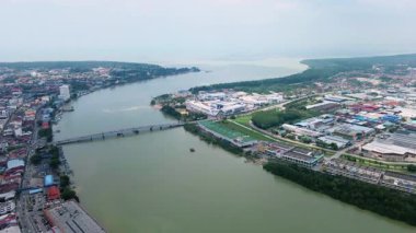 Nehir üzerinde köprüsü olan bir sahil kasabasının havadan görünüşü, endüstriyel binalar, mangrovlar ve arka planda açık deniz..