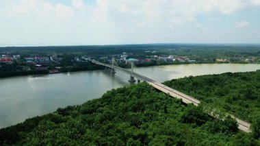 Orman ve binalarla çevrili geniş bir nehri geçen kablo destekli uzun bir köprünün havadan görüntüsü. Modern altyapı.