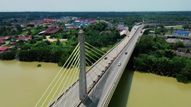 Orman ve binalarla çevrili geniş bir nehri geçen kablo destekli uzun bir köprünün havadan görüntüsü. Modern altyapı.