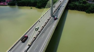 Orman ve binalarla çevrili geniş bir nehri geçen kablo destekli uzun bir köprünün havadan görüntüsü. Modern altyapı.