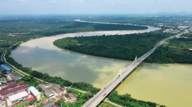 Orman ve binalarla çevrili geniş bir nehri geçen kablo destekli uzun bir köprünün havadan görüntüsü. Modern altyapı.