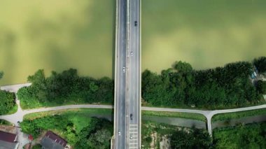 Çamurlu bir nehri geçen, yemyeşil ve yollarla çevrili bir karayolu köprüsünün yukarıdan aşağı görüntüsü. Yukarıdan simetrik kentsel altyapı.
