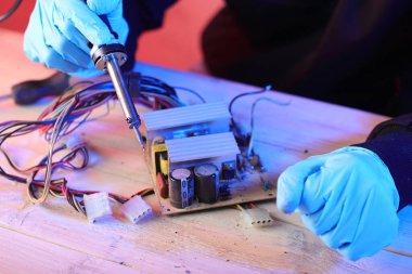 Renkli bir arkaplanda sökülmek için eski bir bilgisayar güç kaynağının lehimlenmesi