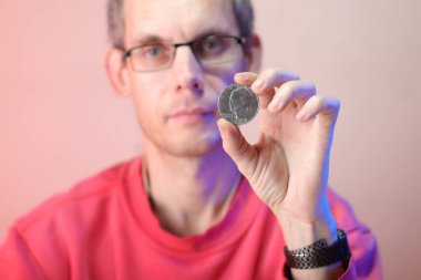 Renkli bir arka planda, sol elinde bozuk para tutan bir adam.