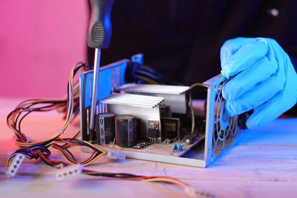 disassembly of a computer power supply on a table by a person and a pink background